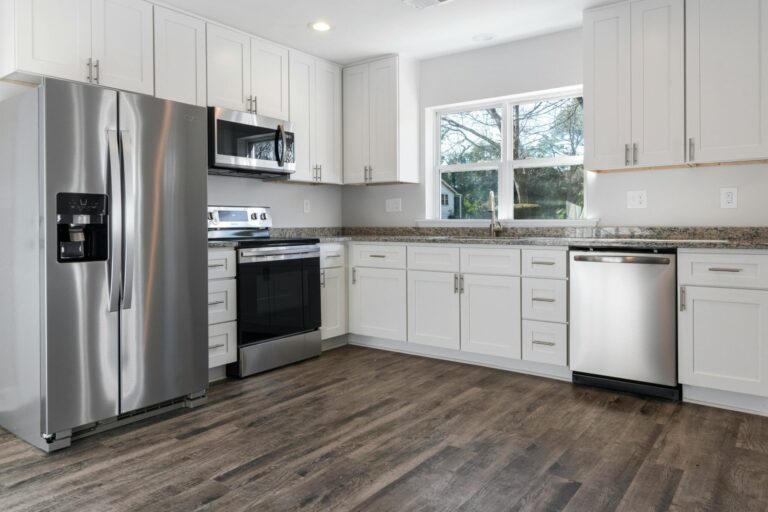 Spotless kitchen with brown wood floors, white cabinets, and silver appliances